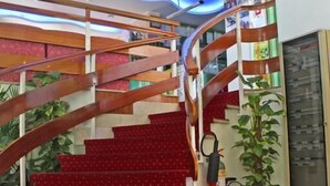A spiral staircase with red carpeted steps and a wooden railing. - Hotel Royal (Misano Adriatico)