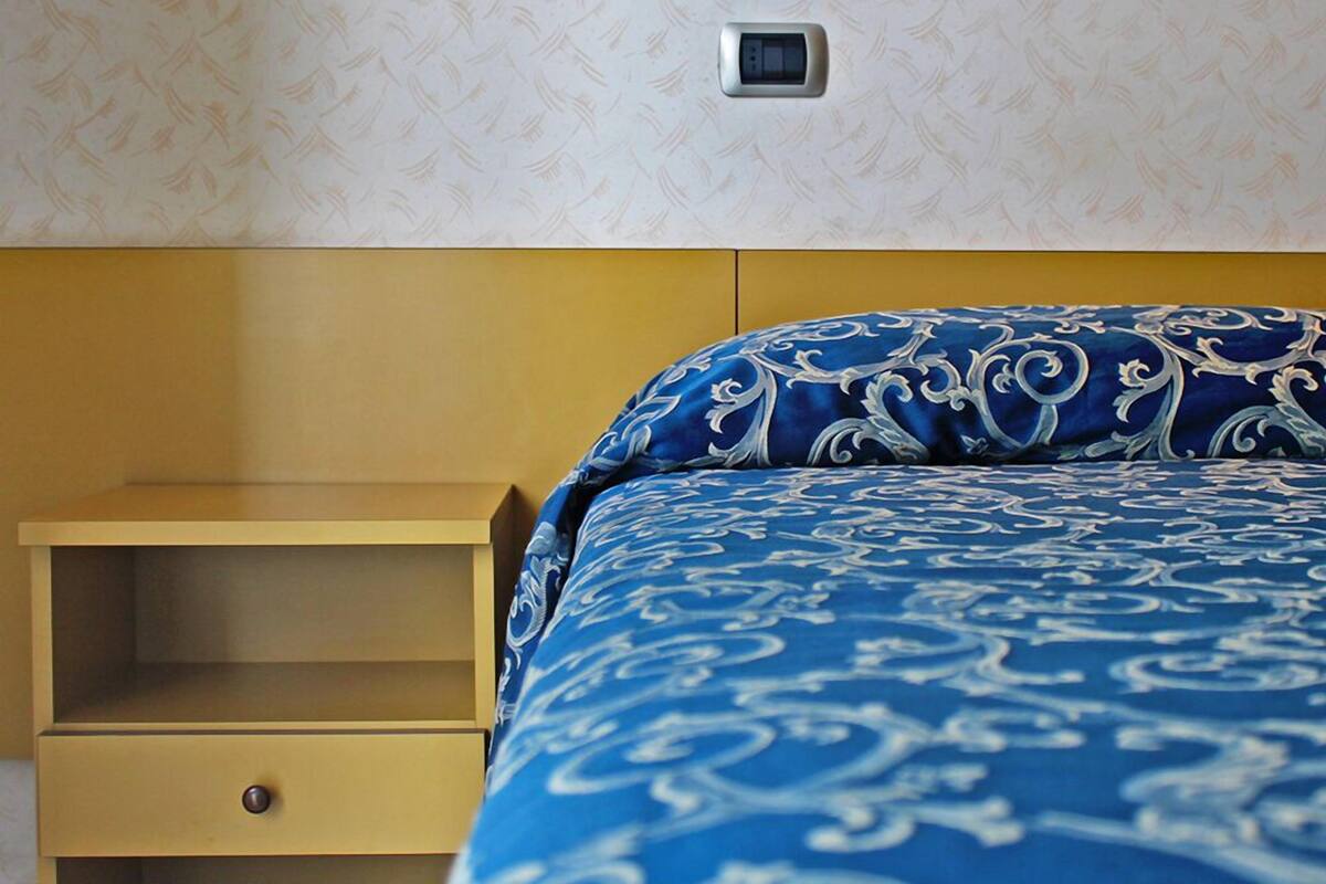 A hotel room with a bed, a bedside table, and a wall-mounted light fixture.