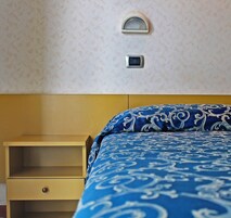 A hotel room with a bed, a bedside table, and a wall-mounted light fixture.