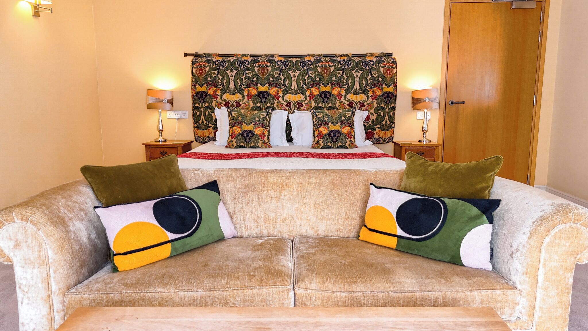 Un dormitorio con cama, dos mesitas de noche, un tapiz y un sofá con cojines decorativos.