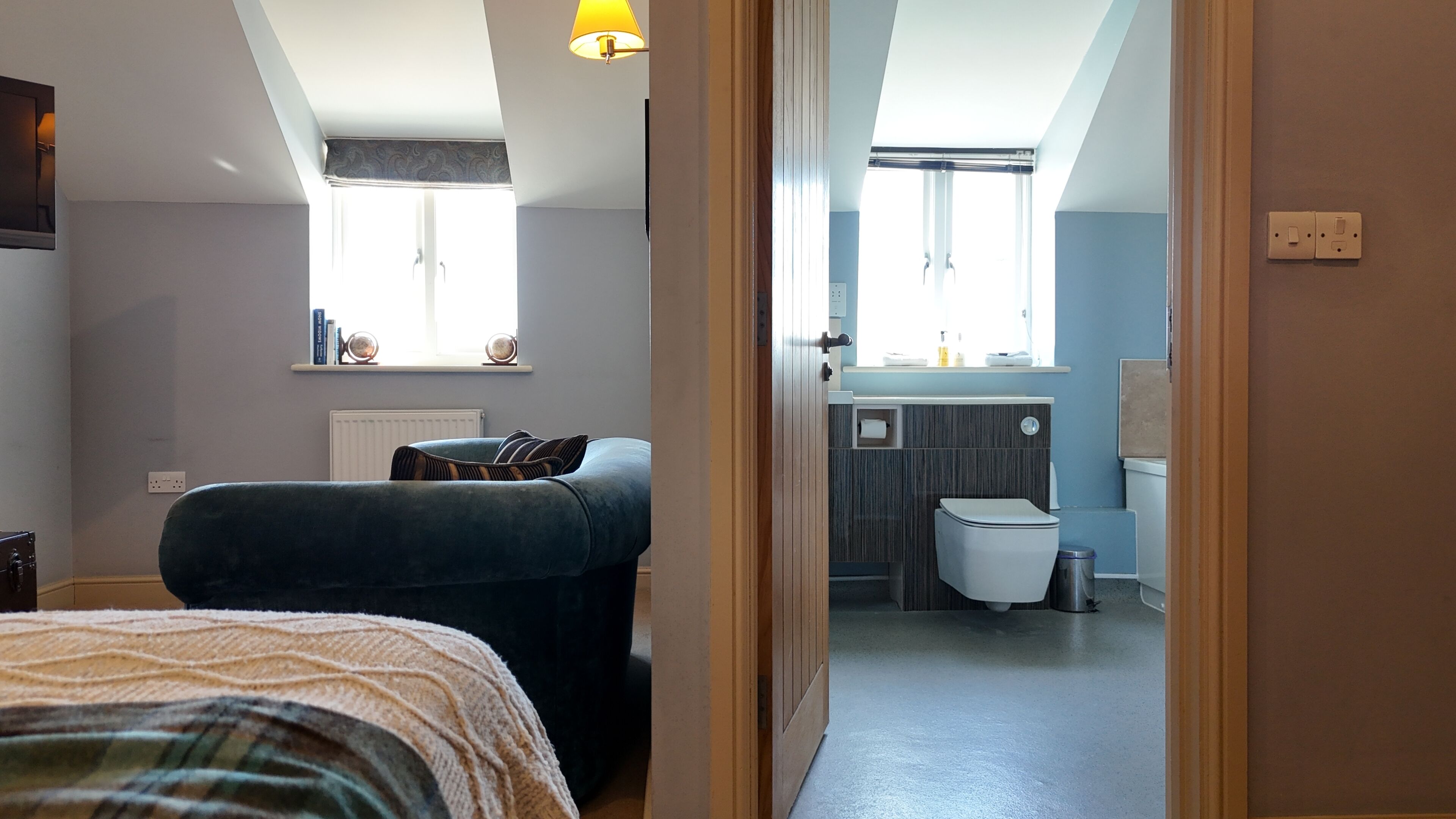 Une chambre à coucher avec un lit, une fenêtre et une vue sur une salle de bain équipée de toilettes et d’un lavabo.