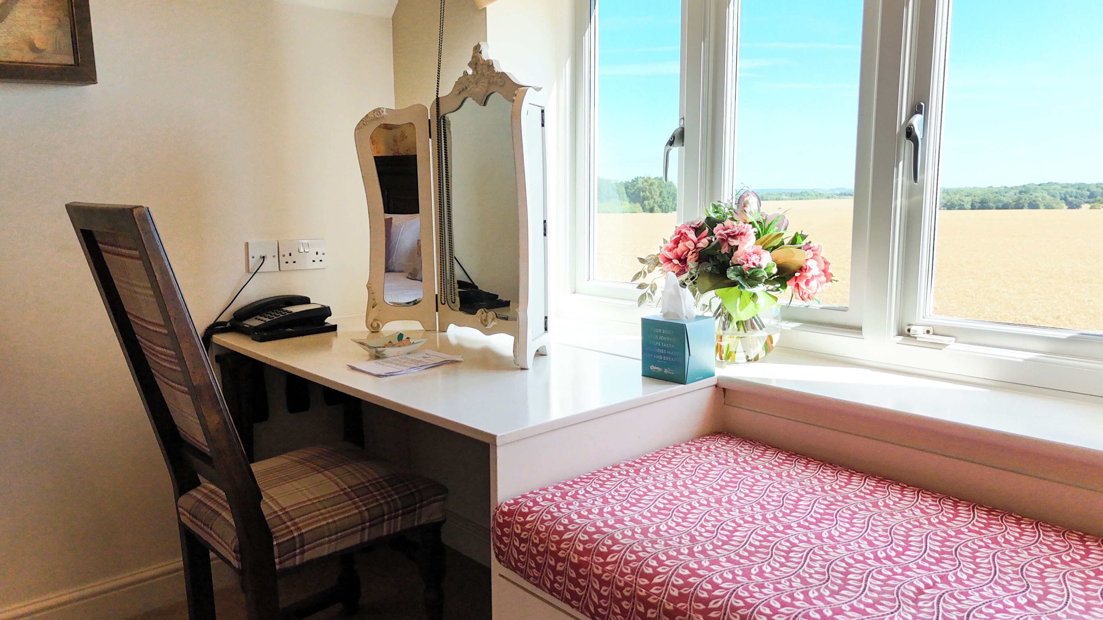A room with a desk, chair, and bench by a window with a view of a beach.