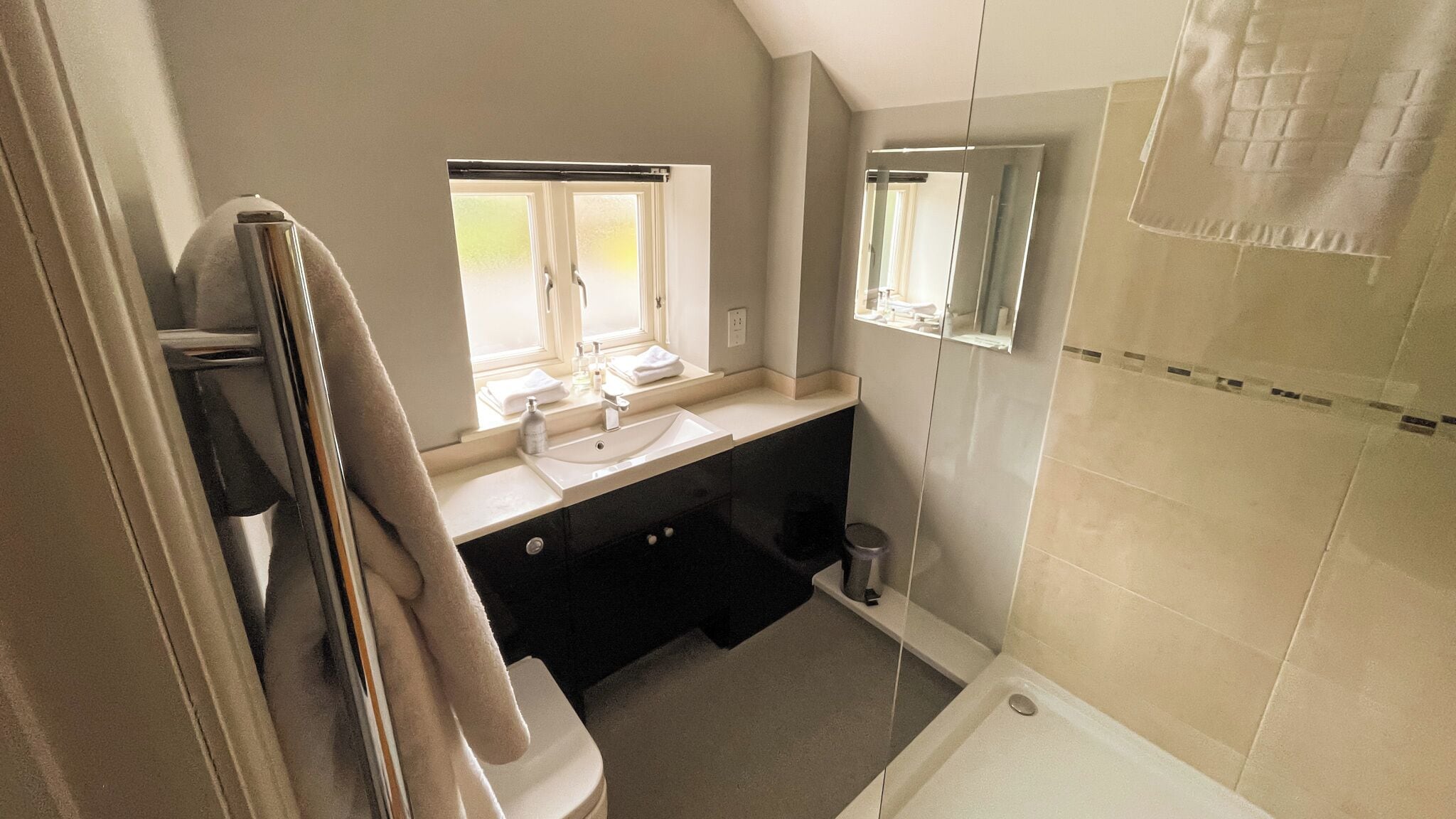 A bathroom with a sink, mirror, window, and shower.