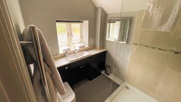 A bathroom with a sink, mirror, window, and shower.