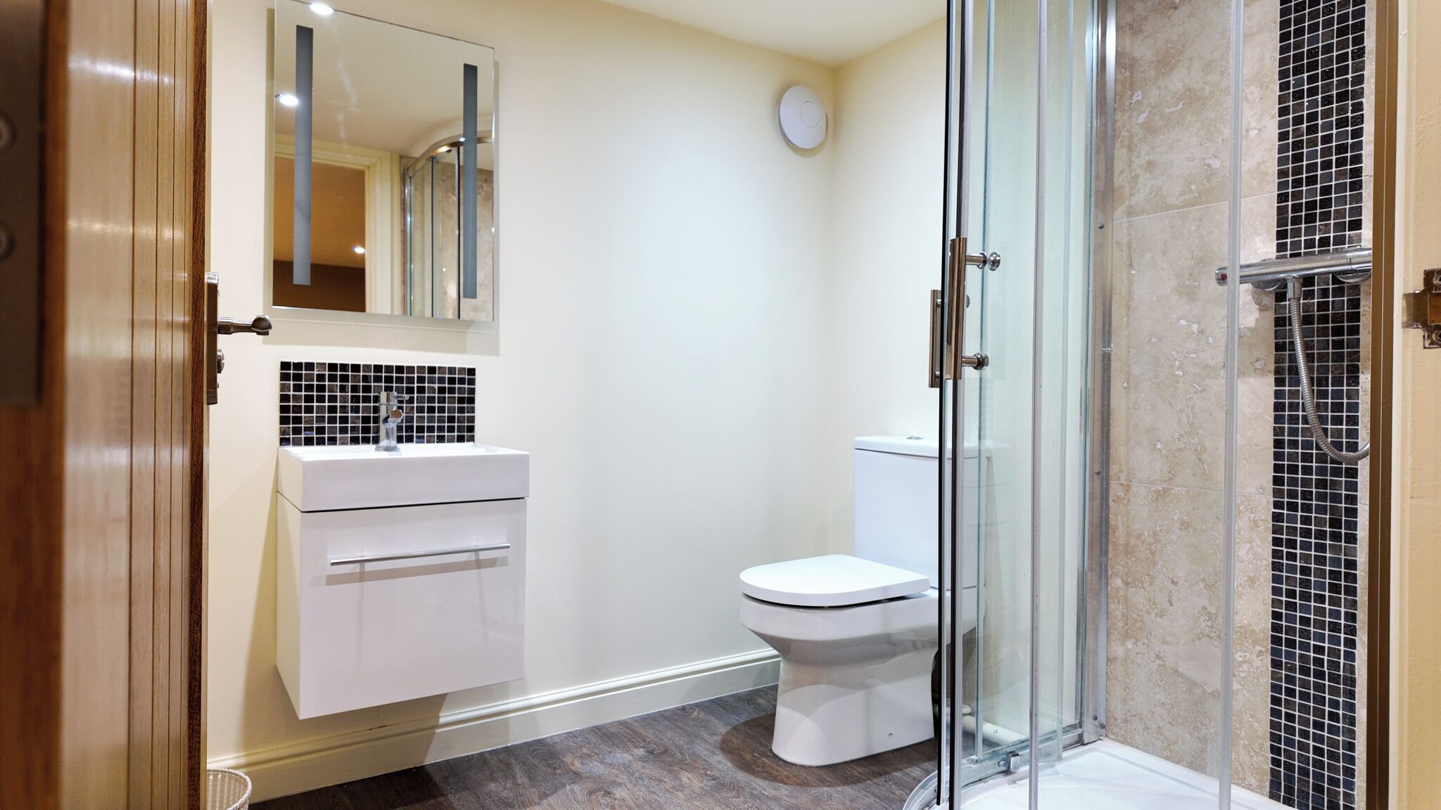 A modern bathroom with a glass shower enclosure, a white toilet, and a vanity with a mirror and sink.