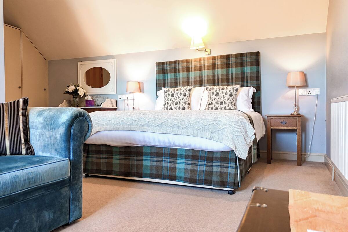 A bedroom with a bed, a blue sofa, a nightstand with a lamp, and a dresser.