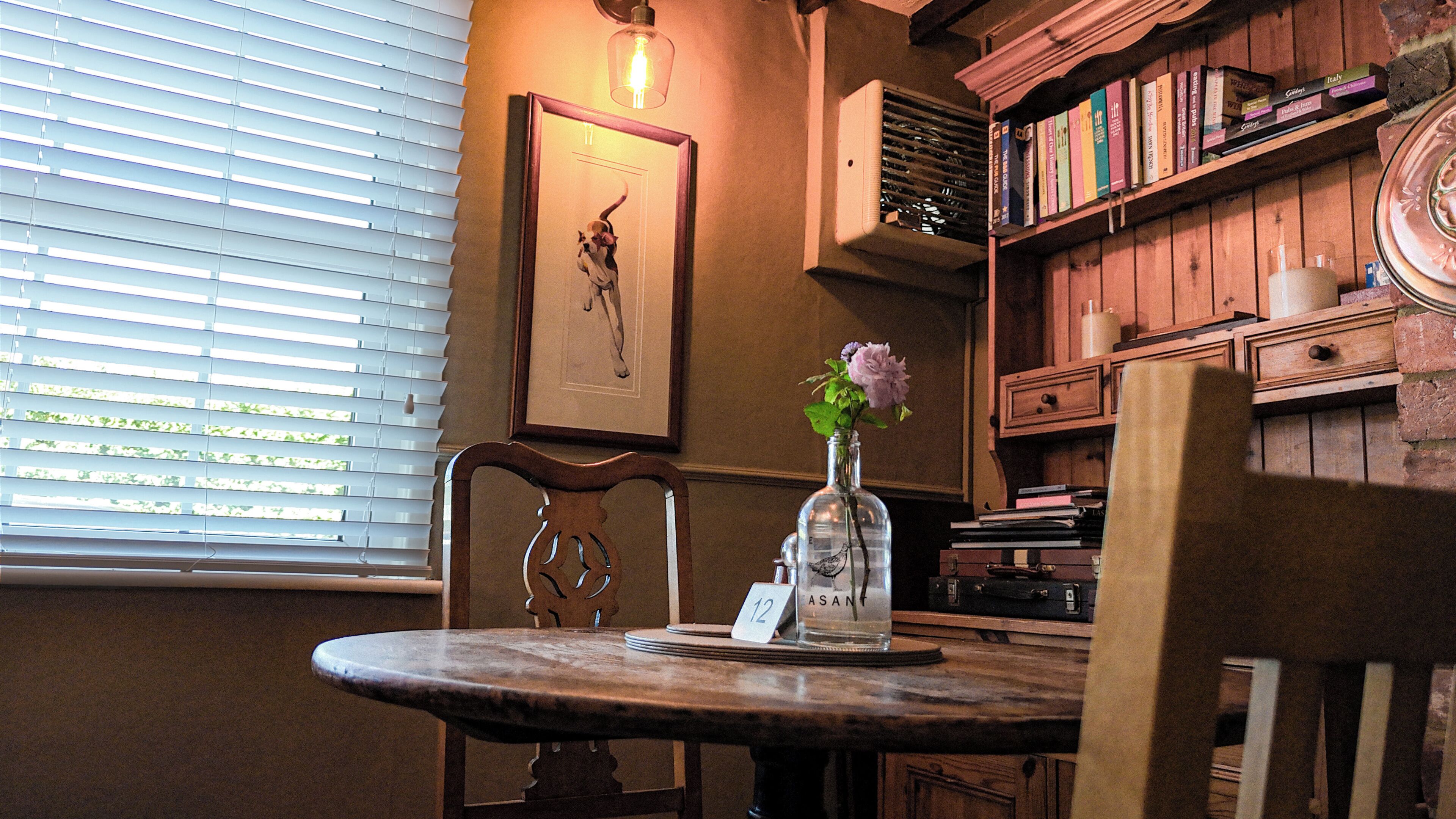 A dining table with a vase of flowers, a framed picture on the wall, and a bookshelf with books.