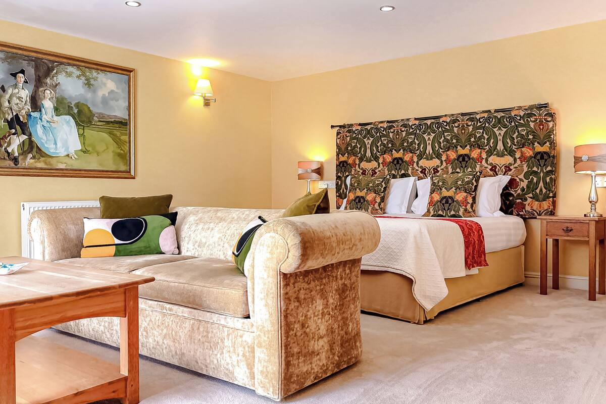 A room with a bed, a sofa, a table, and a painting on the wall.
