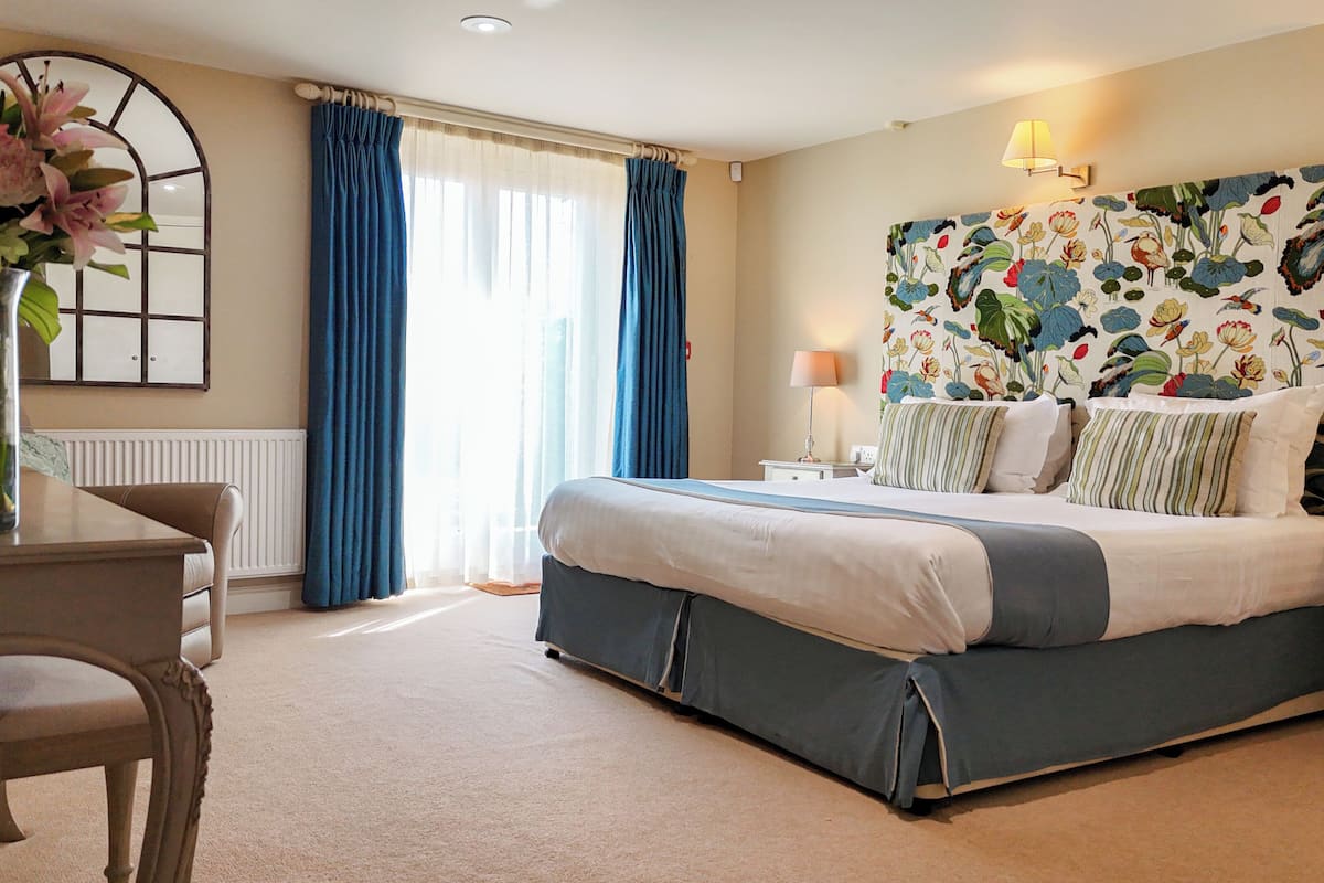 A hotel room with a bed, a desk, a chair, a lamp, and a floral wallpaper.