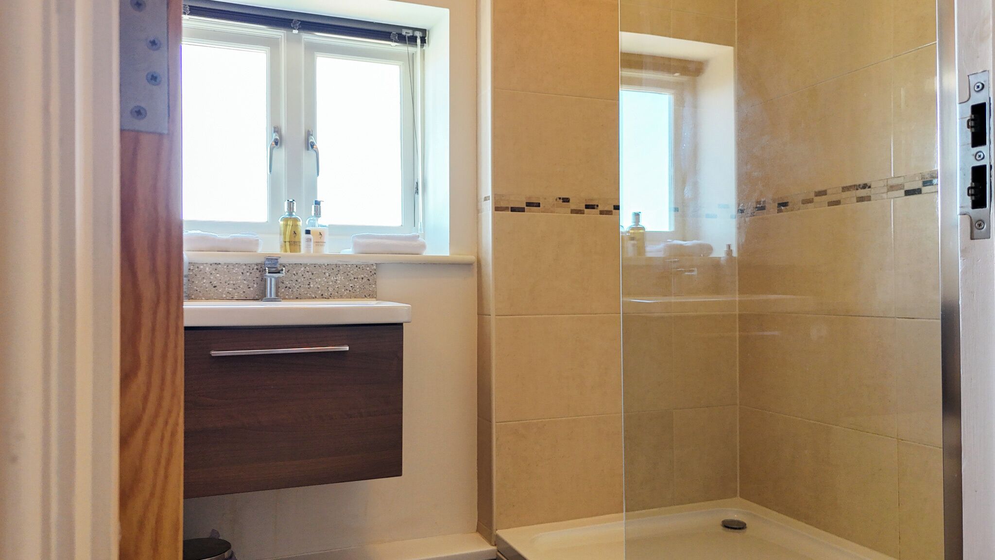 A bathroom with a shower, a window, and a vanity with a sink.