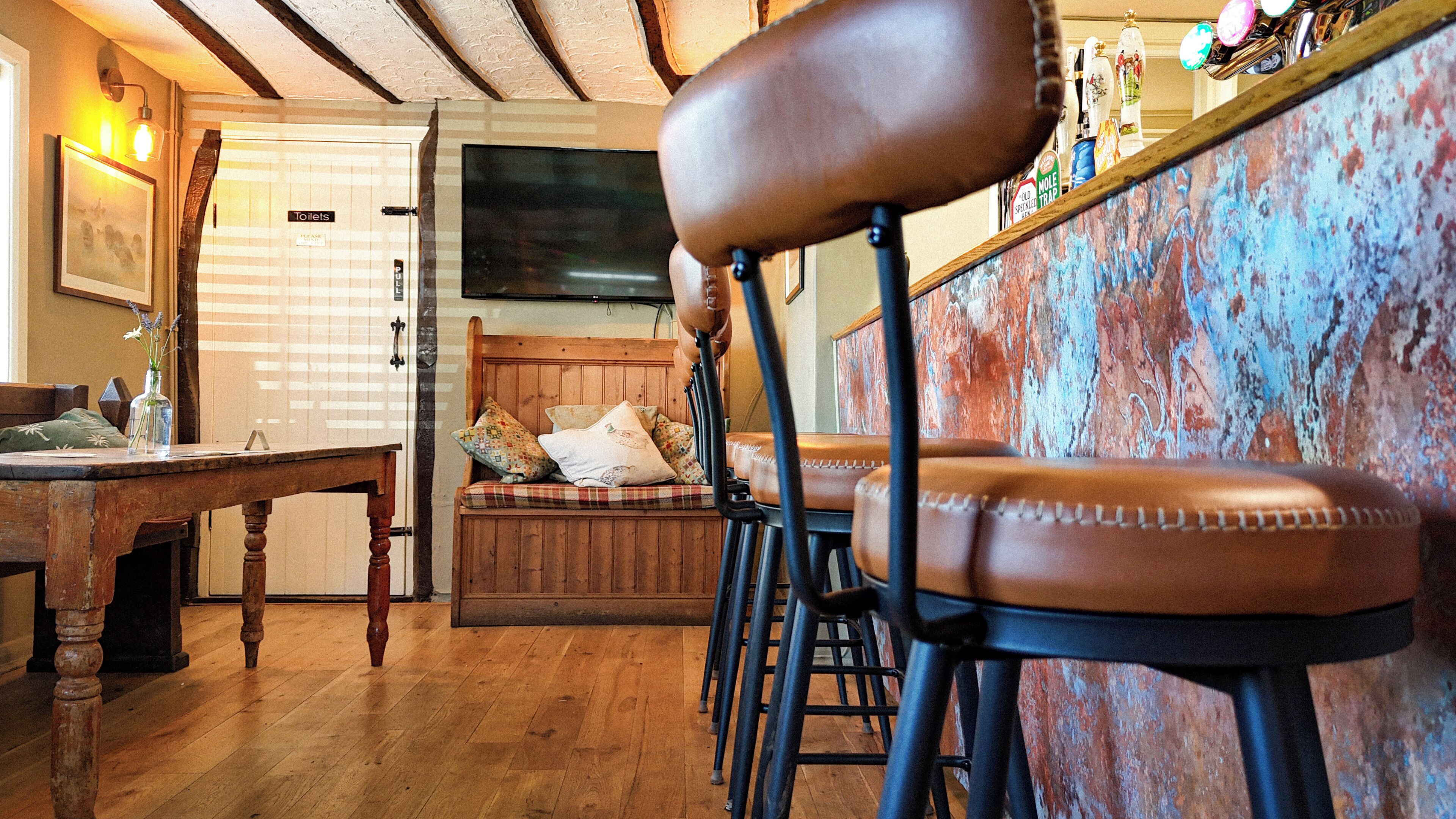 Een bar met barkrukken, een houten bank en een aan de muur bevestigde televisie.