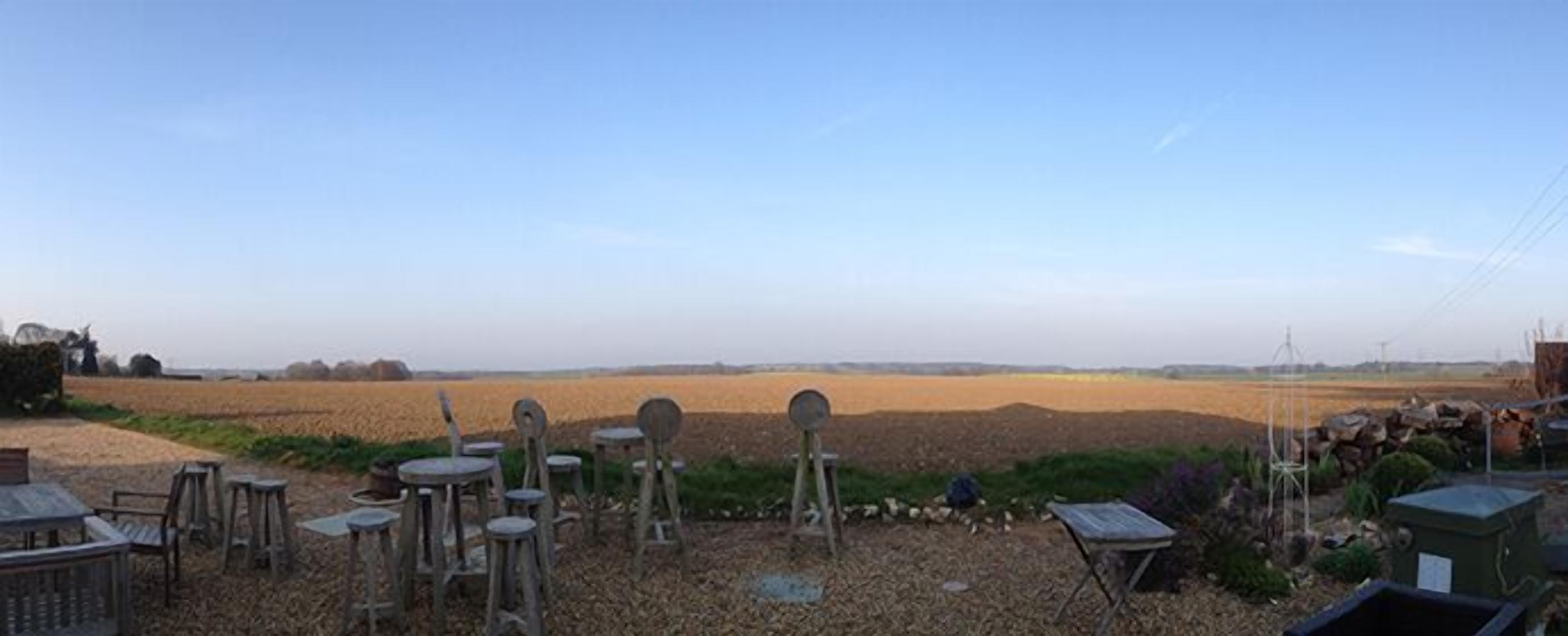Un ambiente rurale all'aperto con un campo, tavoli e sedie sparsi, e una piccola costruzione.