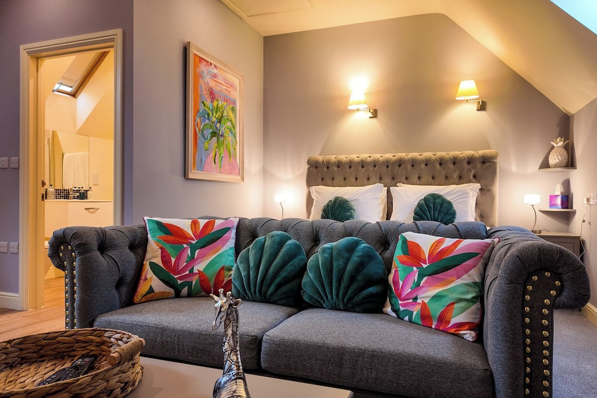 A cozy living room with a grey sofa, colorful pillows, a giraffe sculpture, and a painting on the wall.