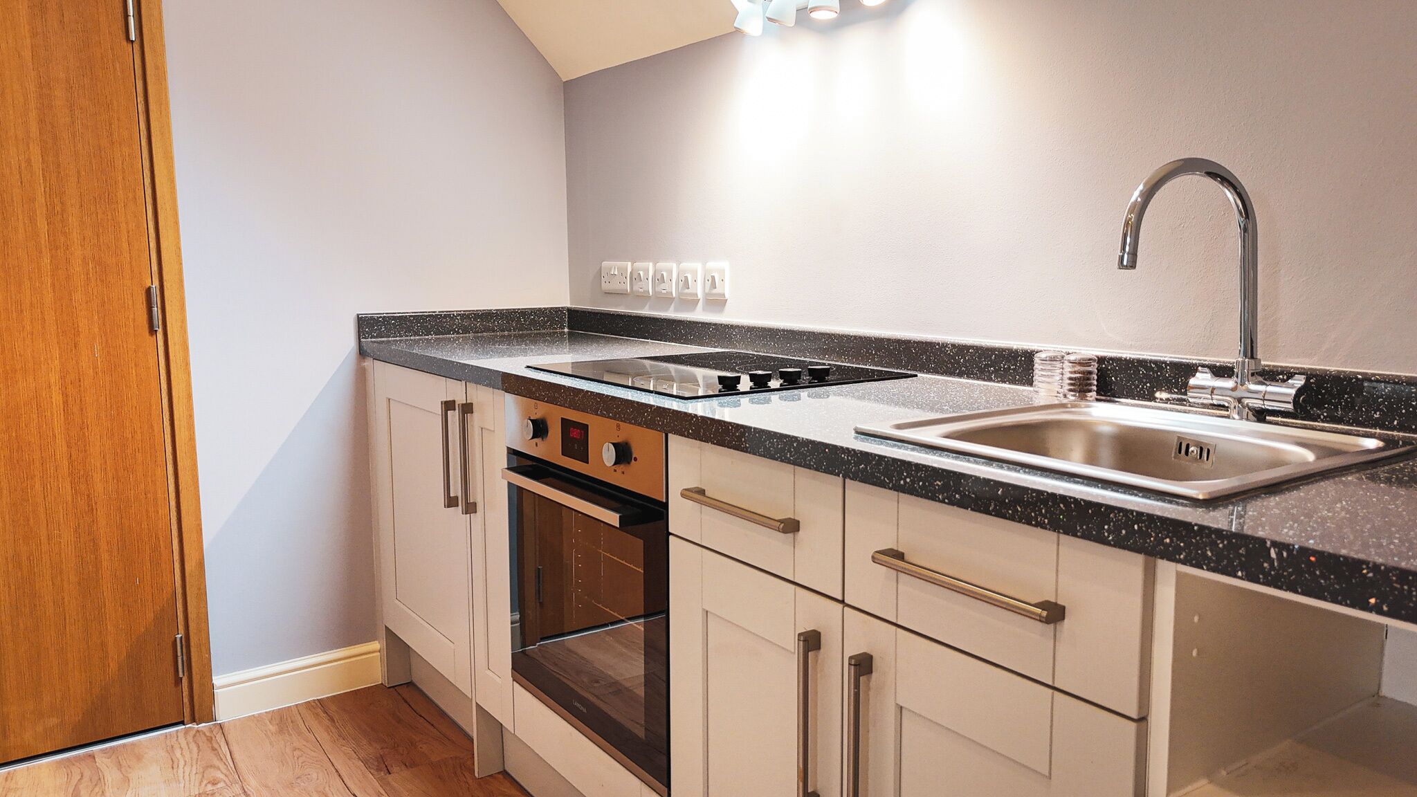 A compact kitchen with a stove, oven, sink, and wooden cabinets.