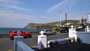 A coastal road with parked cars and a white building with a balcony. - Kittiwake House (Port Erin)