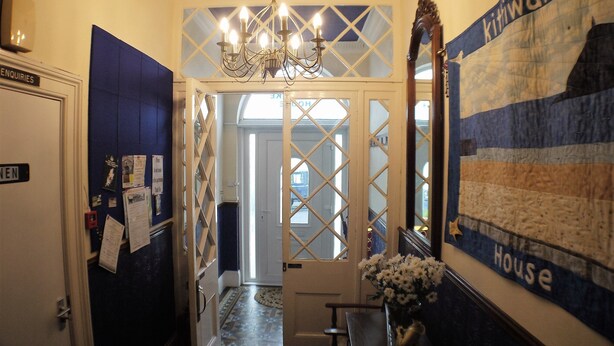 A hallway with a chandelier, a blue wall with a 'House' sign, and a door labeled 'Enquiries'. - Kittiwake House (Port Erin)