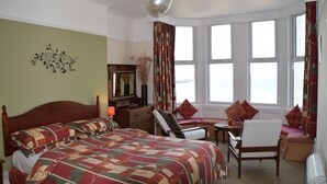 A hotel room with a large bed, a desk with a chair, a window with curtains, and a decorative wall piece. - Kittiwake House (Port Erin)