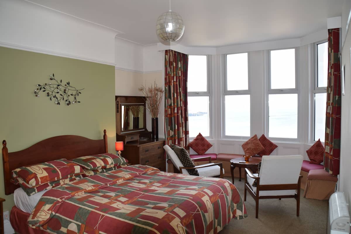Ett hotellrum med en stor säng, ett skrivbord med en stol, ett fönster med gardiner och en dekorativ väggdekoration.