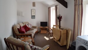 A living room with a sofa, a TV, a desk, and a washing machine. - Kittiwake House (Port Erin)