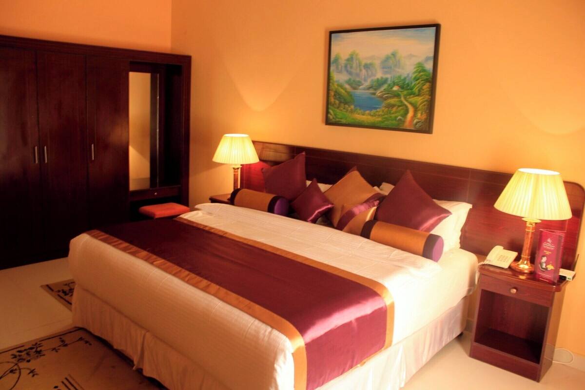 A hotel room with a large bed, two bedside lamps, a nightstand with a phone, and a painting on the wall.