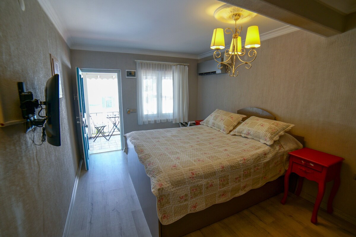 A bedroom with a bed, a red nightstand, a chandelier, and a door leading to a balcony.