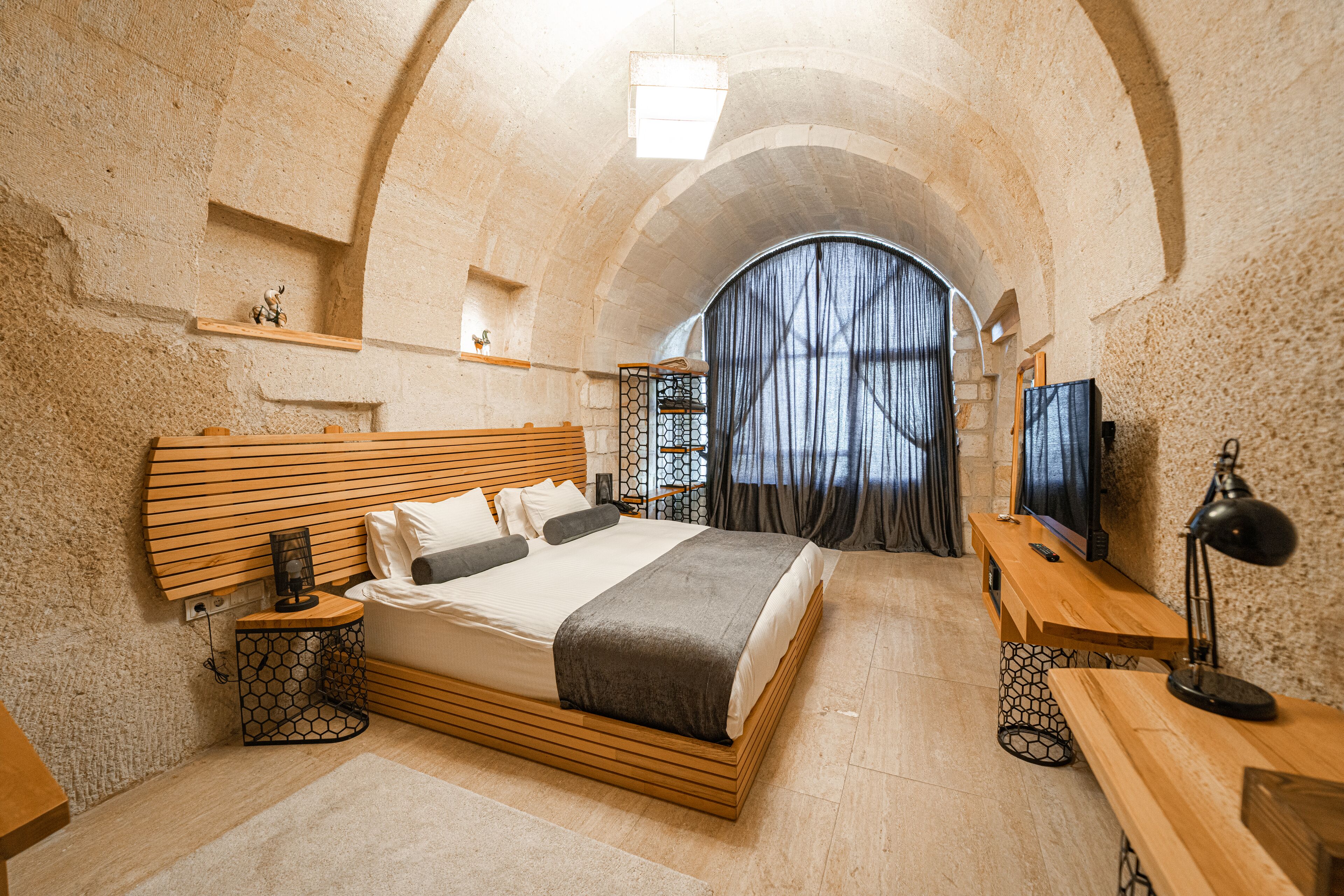 A bedroom with a wooden bed, a TV, a desk, and a window with curtains.