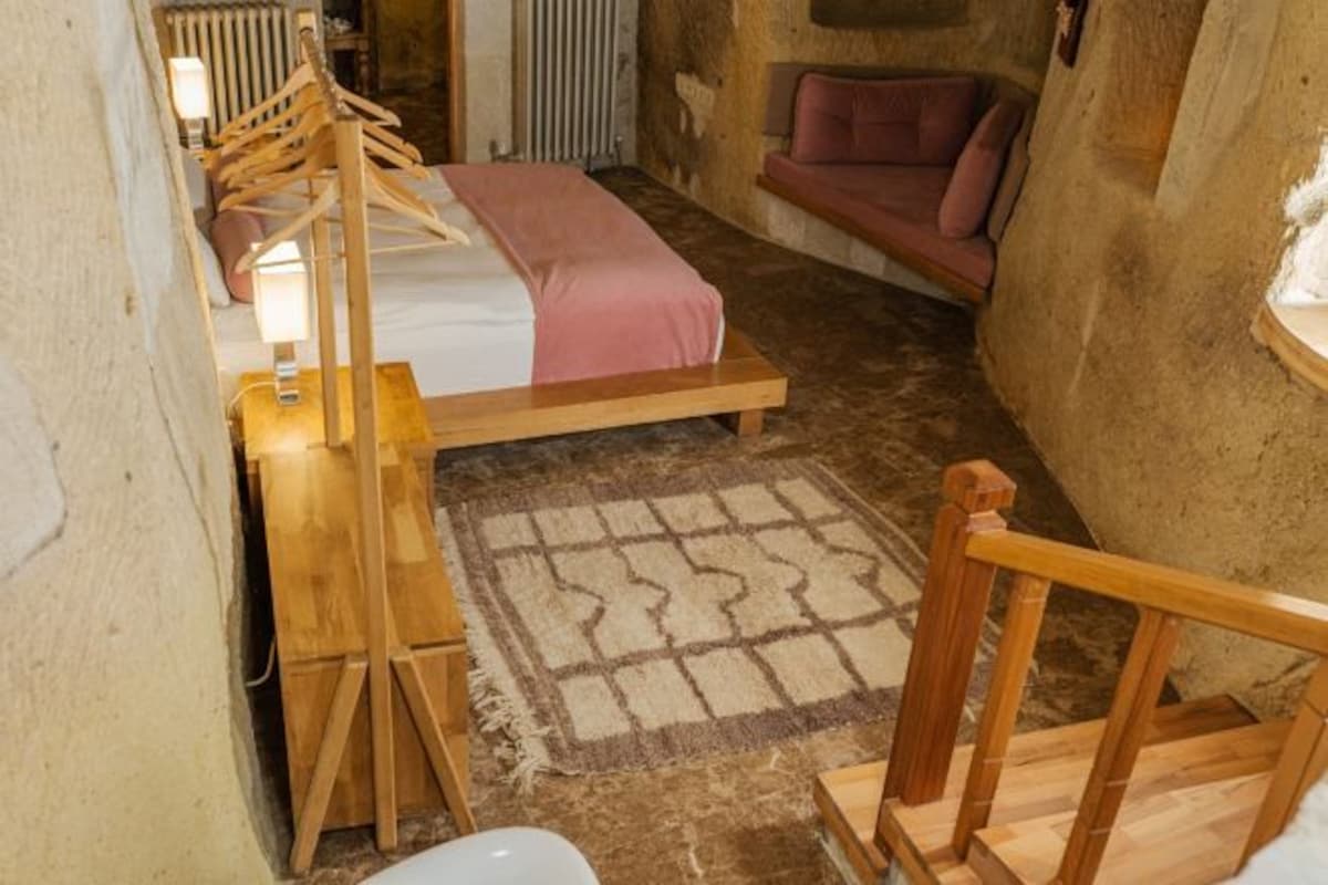 A rustic room with a bed, wooden furniture, a patterned rug, and a stone wall.