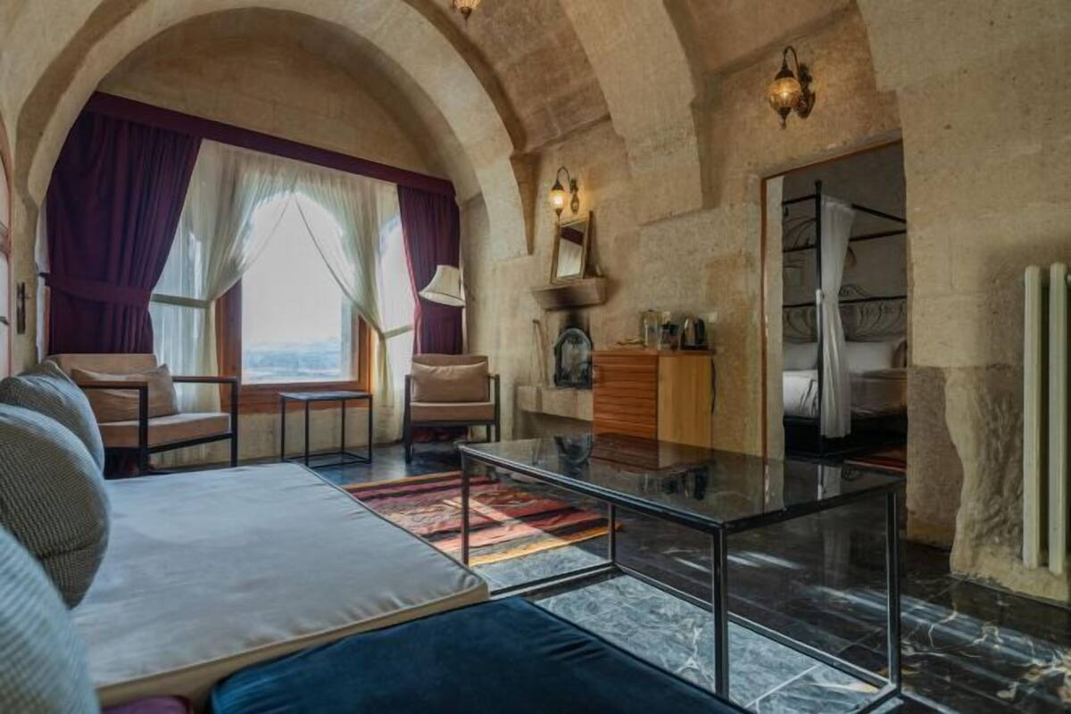 Una habitación amplia con una cama grande, zona de estar y vistas a través de un ventanal de arco.