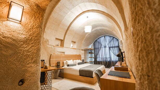 Un dormitorio acogedor con techo abovedado de piedra, una cama de madera, un escritorio y una silla.