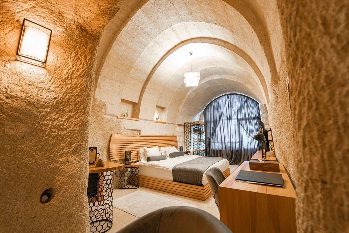 Un dormitorio acogedor con techo abovedado de piedra, una cama de madera, un escritorio y una silla.