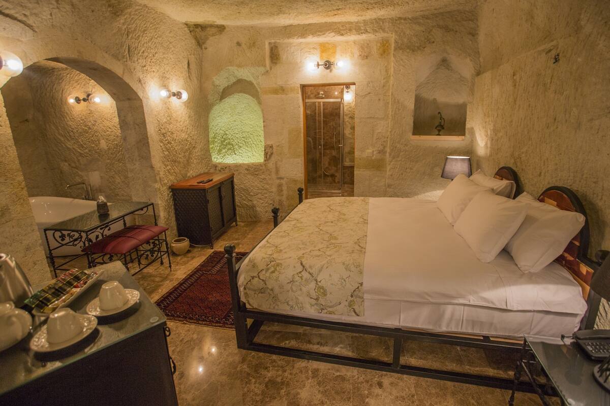Un dormitorio con paredes de piedra, una cama, una mesita de noche, una ventana y una puerta.