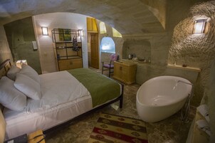A bedroom with a bed, a large bathtub, a chair, and a small table.