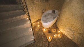 Una bañera en un ambiente tipo cueva, con un taburete de madera y un adorno en el suelo.