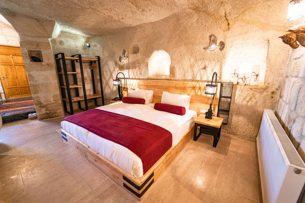 Un dormitorio acogedor con una cama de madera, un plaid rojo y una mesita de noche con una lámpara.