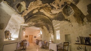 Un interior rústico con paredes de piedra, techos abovedados y mesas dispuestas para comer.