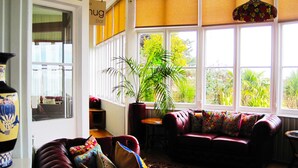 A cozy living room with a red sofa, a large window with a view of greenery, and a hanging light fixture. - The Clifton (Shanklin)