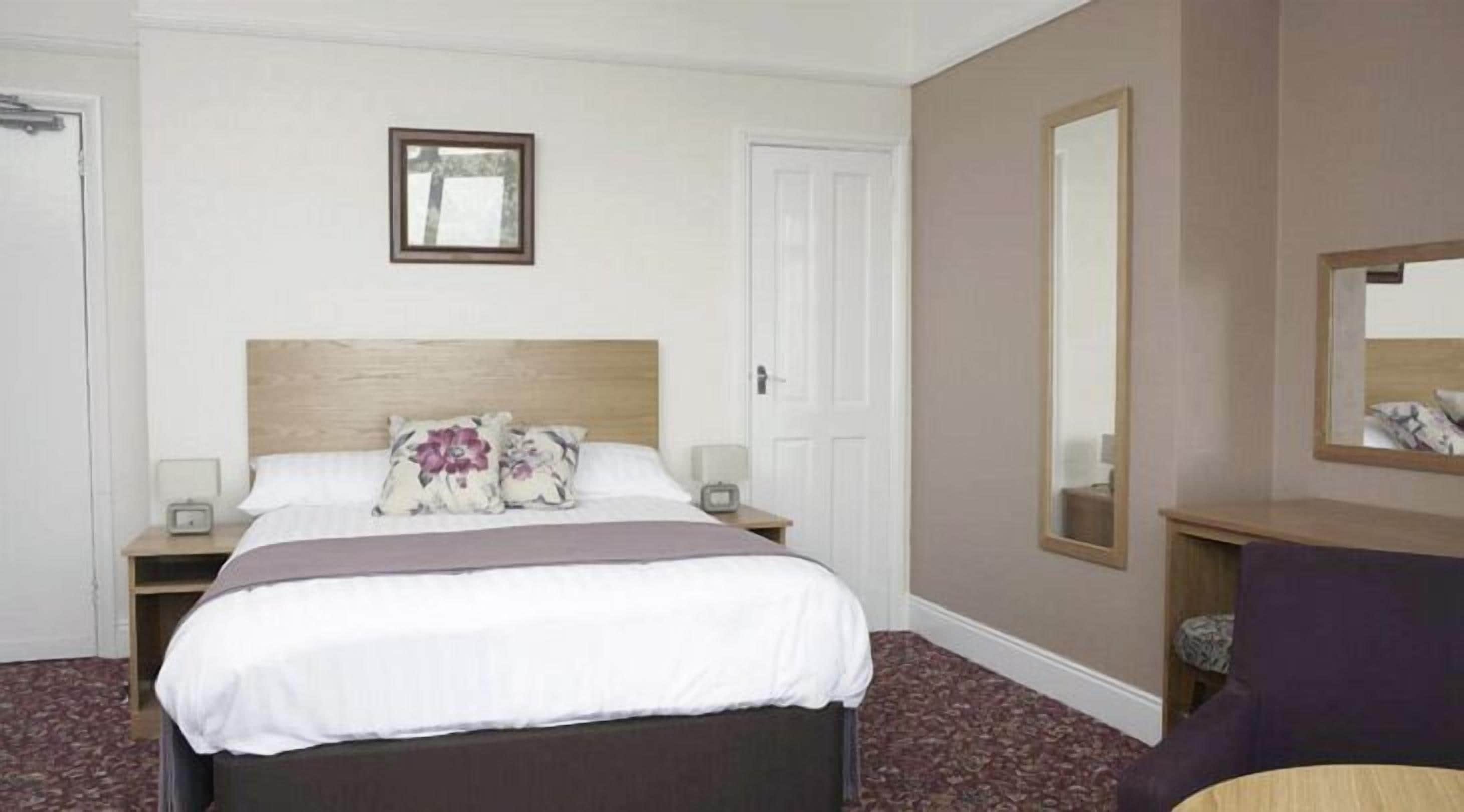 A hotel room with a bed, bedside tables, a nightstand, a mirror, and a chair.
