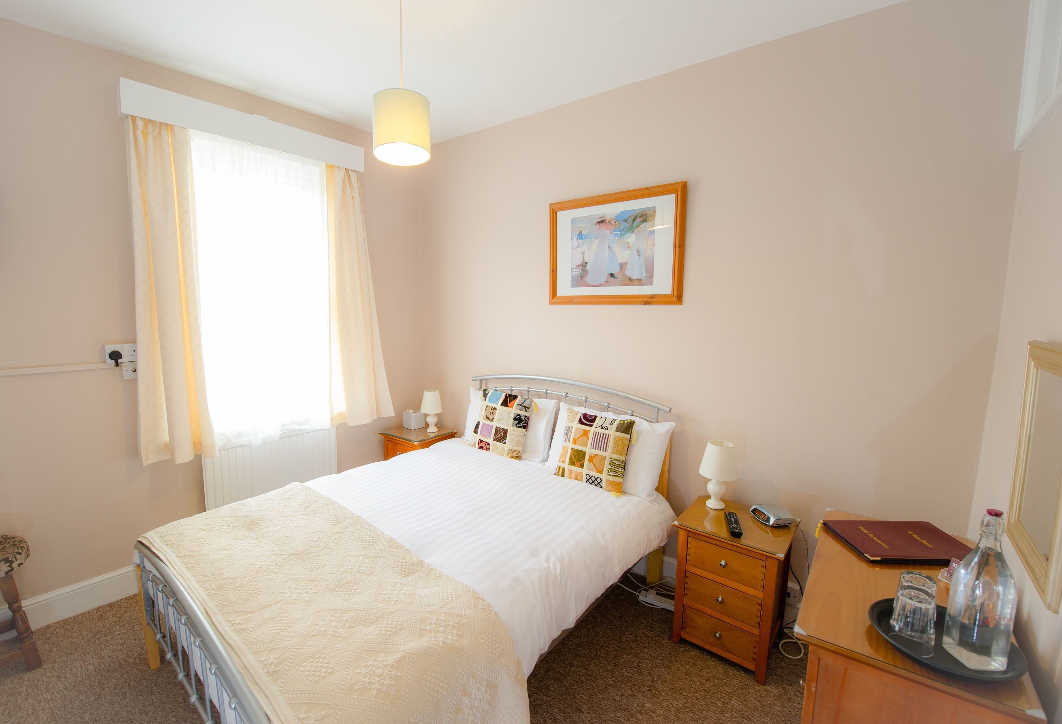 A neatly arranged bedroom with a bed, bedside tables, a nightstand, a dresser, and a framed picture on the wall.