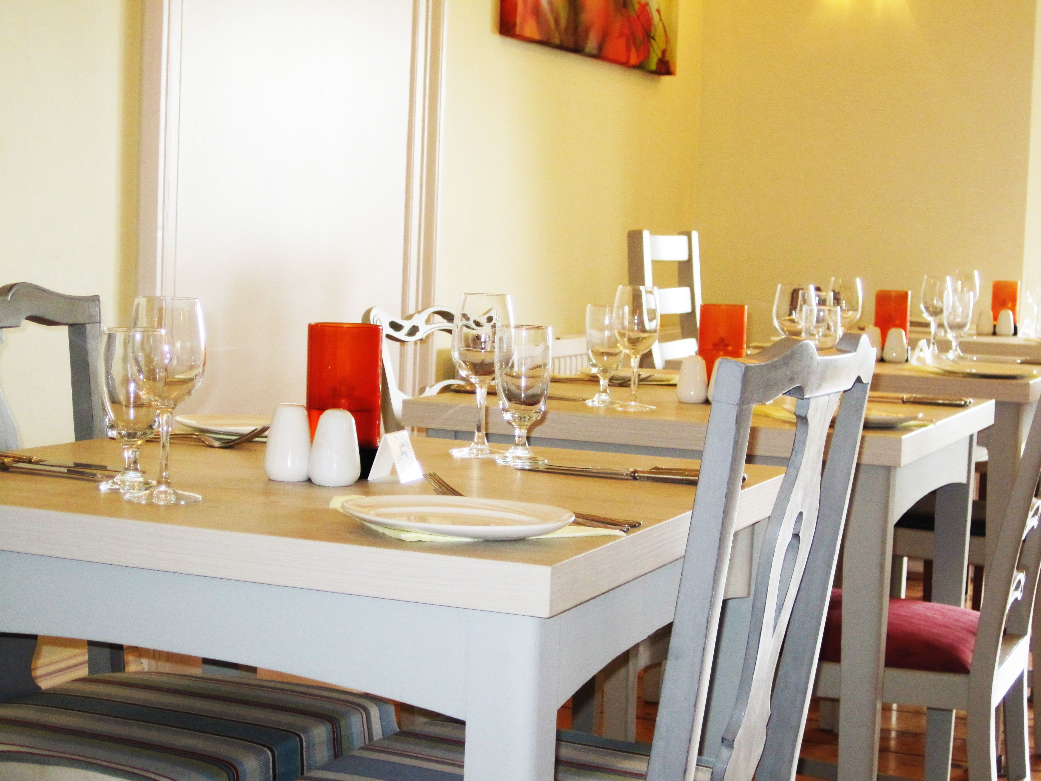 A dining area with tables set for two, each with wine glasses, plates, and cutlery.