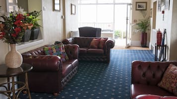 Ein Zimmer mit Teppichmuster, Ledersofas, einem kleinen Tisch mit einer Vase und einem großen Fenster mit Blick.