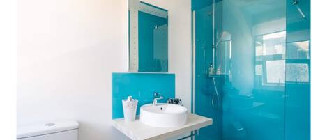 A modern bathroom with a white sink, a mirror, and a glass-enclosed shower.