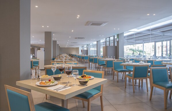 Un restaurante amplio con varias mesas y sillas, ventanas grandes y un diseño interior moderno.