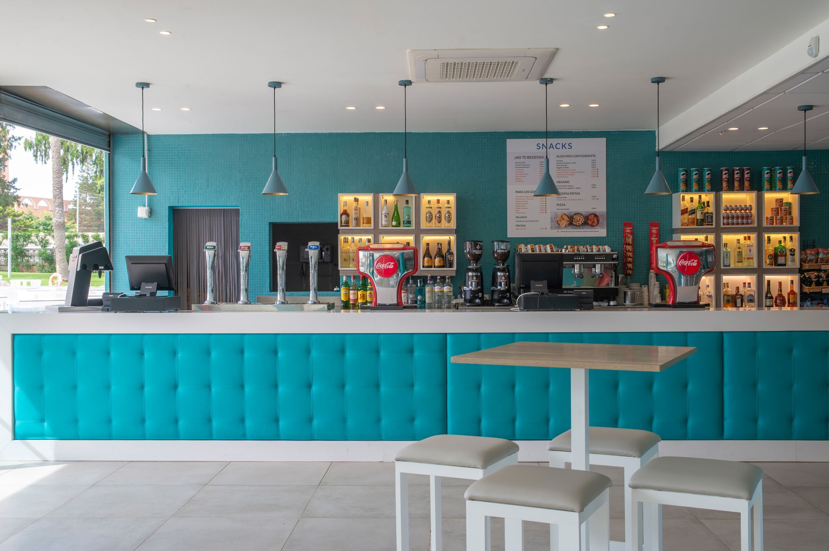 A bar area with a teal-colored counter, multiple hanging lights, and a menu board.