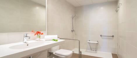 Un baño moderno con lavamanos, inodoro y zona de ducha blancos.