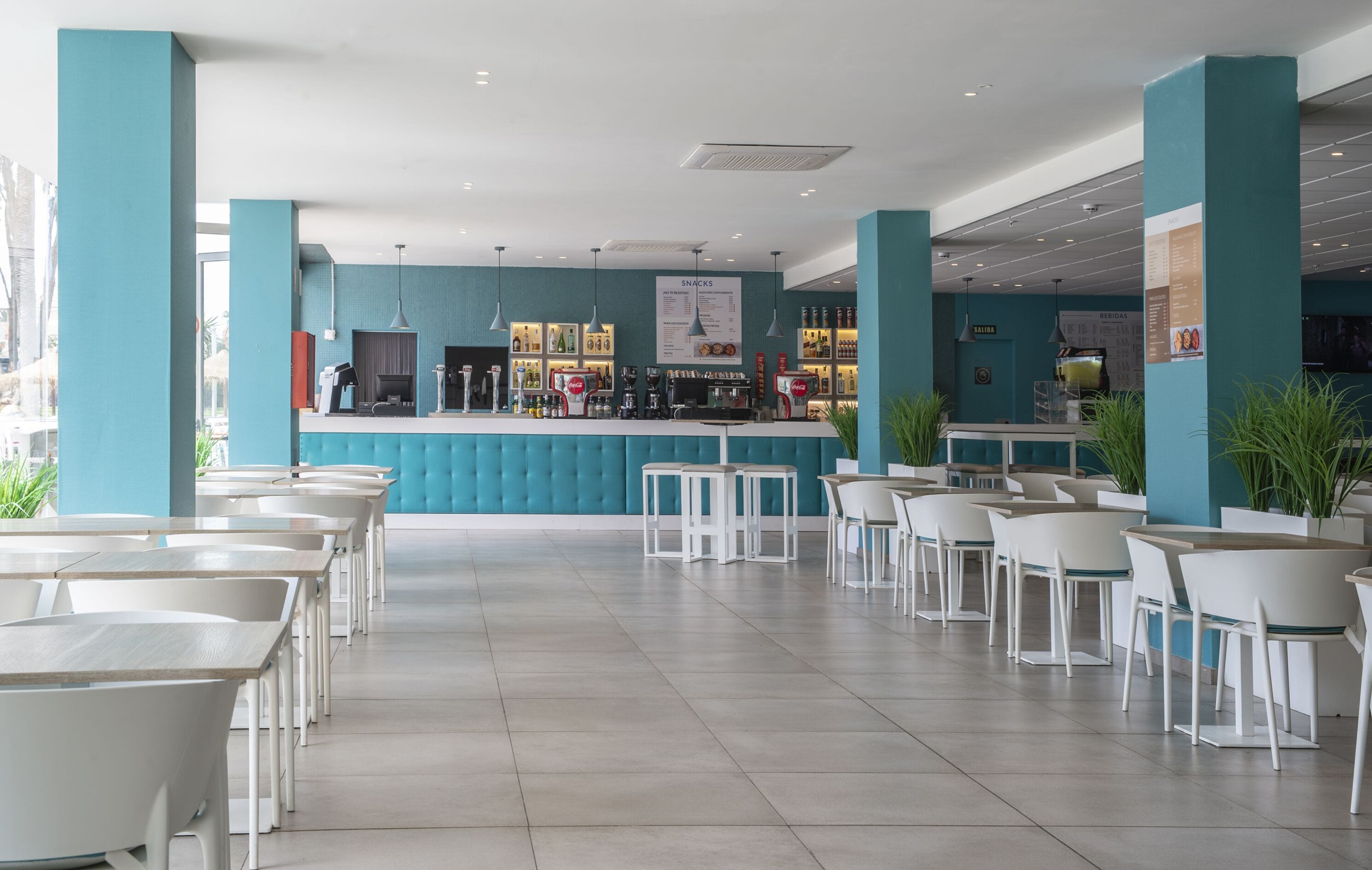 Een modern café met een blauwgroene toonbank, witte stoelen en een betegelde vloer.