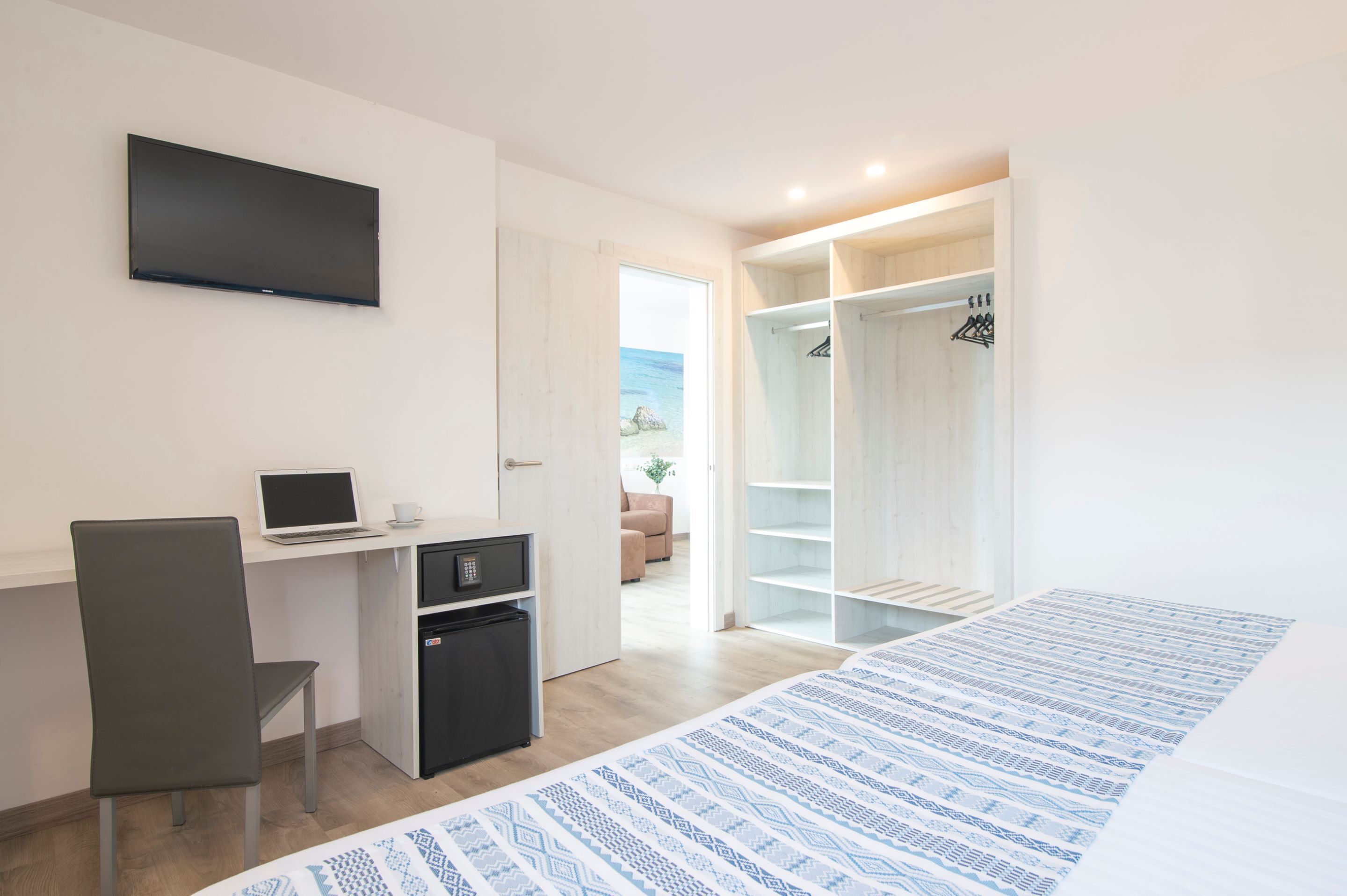 Moderni hotellihuone, jossa on työpöytä, kannettava tietokone ja kuvioitu päiväpeitteellä varustettu sänky.