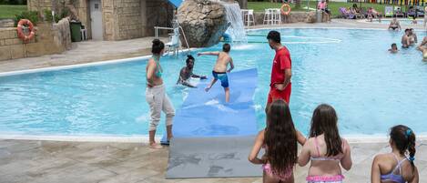 Una piscina con una formación rocosa, sillas de descanso y un flotador salvavidas.