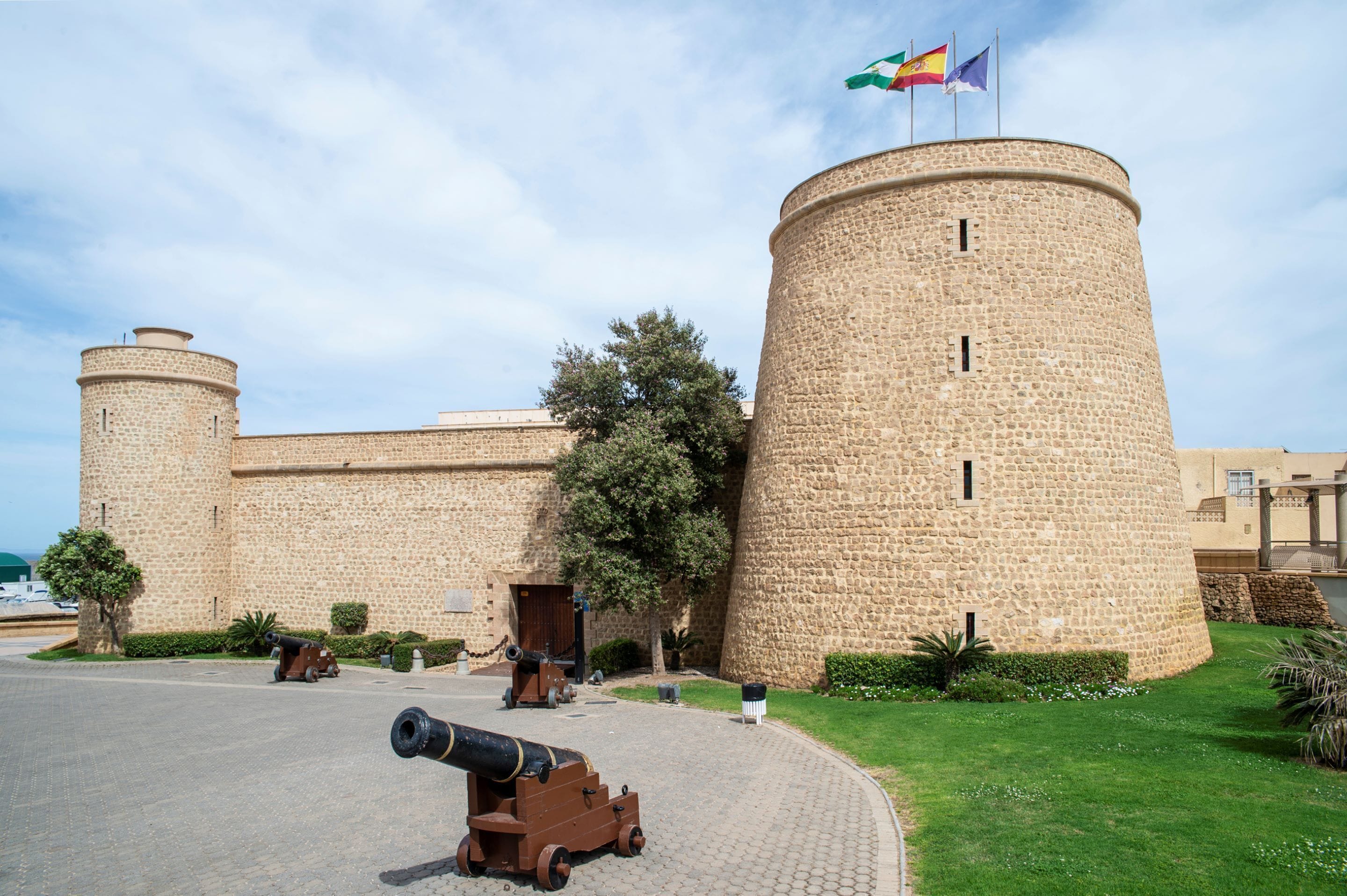 A historic stone castle with a round tower, a flag, and cannons.