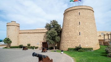 Et historisk stenhus med et rundt tårn, et flag og kanoner.