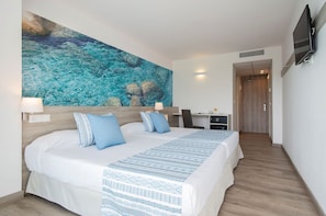 Ein Hotelzimmer mit einem großen Bett, einem Schreibtisch, einem Fernseher und einem Gemälde, das eine blaue Meereslandschaft zeigt.